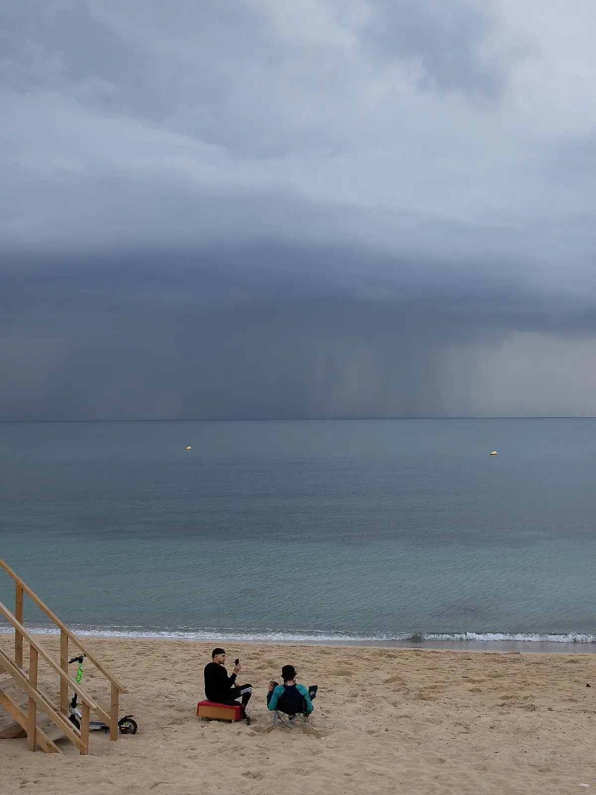 Menschen sitzen am Strand von Can Pere Antoni auf Mallorca und schauen auf eine Regenfront. Für die nächsten 24 Stunden ist auf Mallorca eine Wetterwarnung wegen Regen und Sturm ausgerufen worden.