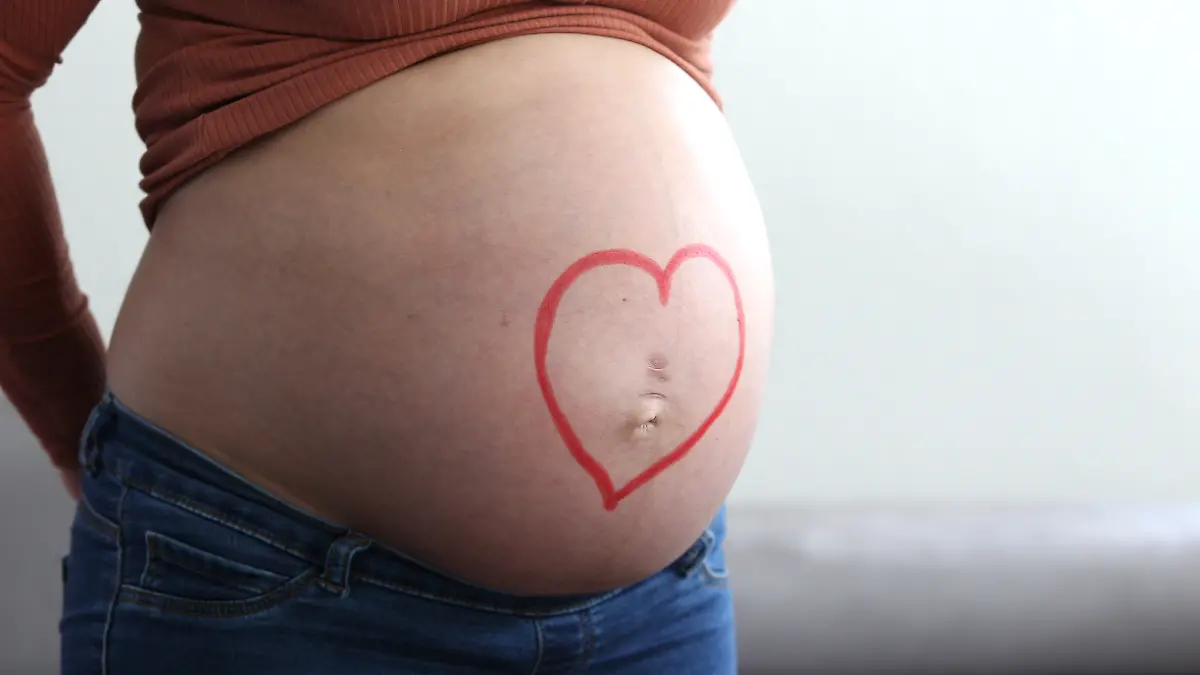 Themenbild - schwangere Frau mit Babybauch, dickem Bauch, Schwangerschaftsbauch Bild: XMR, schwangere Frau mit Babybauch, zeigt ihren dicken Bauch. Auf dem Babybauch liegen Hände und Finger, sowie Babyschuhe mit Geld, Kindergeld, Lachgesicht, Symbolbild, Themenbild, Featurebild || Modellfreigabe vorhanden