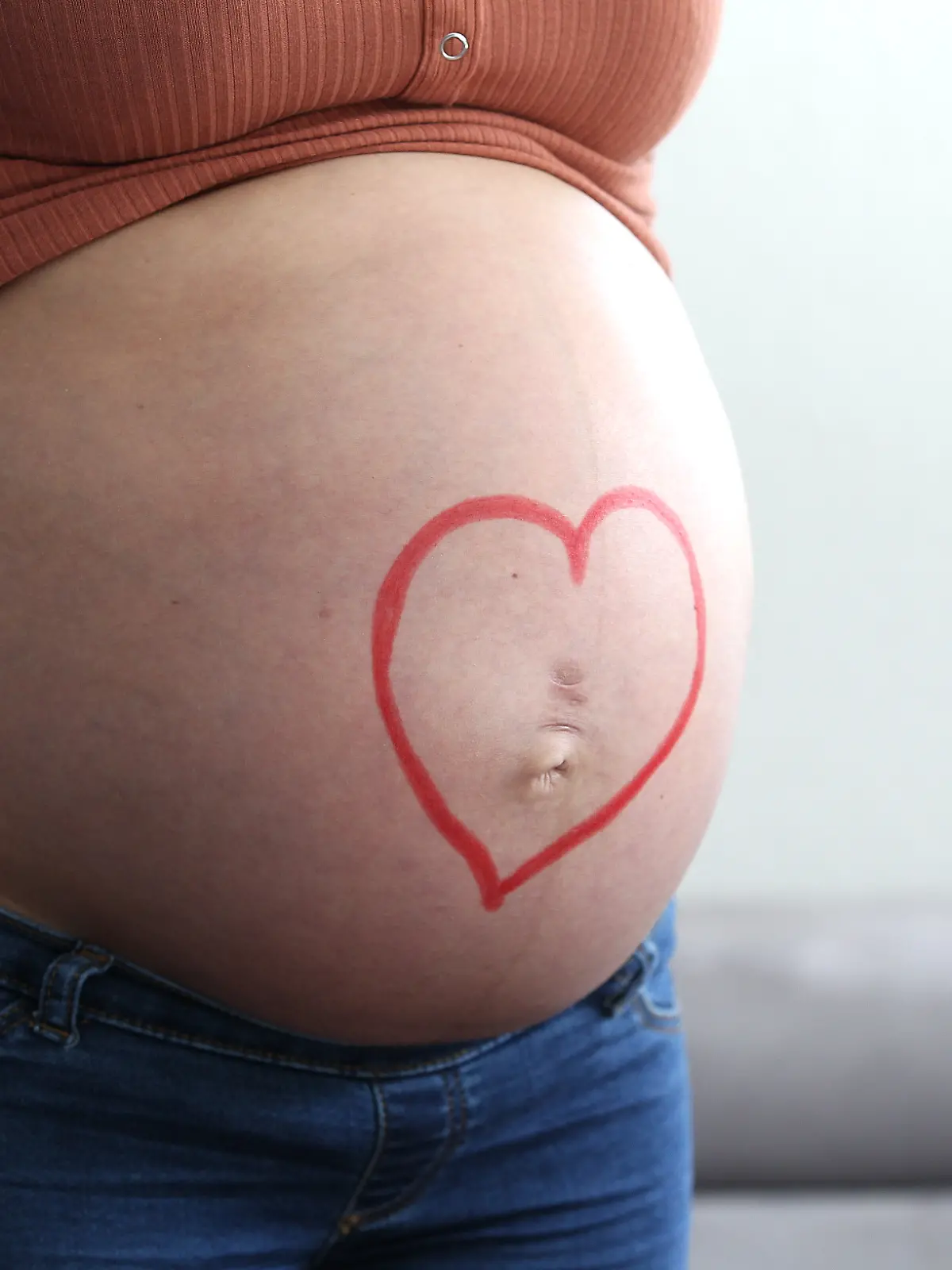 Themenbild - schwangere Frau mit Babybauch, dickem Bauch, Schwangerschaftsbauch Bild: XMR, schwangere Frau mit Babybauch, zeigt ihren dicken Bauch. Auf dem Babybauch liegen Hände und Finger, sowie Babyschuhe mit Geld, Kindergeld, Lachgesicht, Symbolbild, Themenbild, Featurebild || Modellfreigabe vorhanden