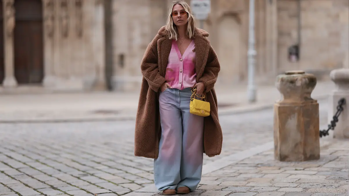 Frau trägt 2000-er Outfit mit Cardigan, Mantel, Sonnenbrille. 