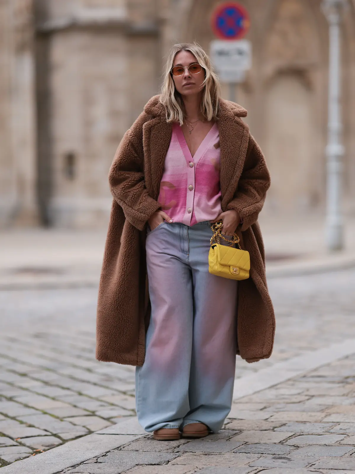 Frau trägt 2000-er Outfit mit Cardigan, Mantel, Sonnenbrille. 