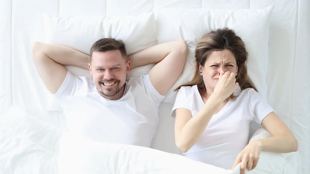 Frau liegt im Bett mit Mann und bedeckt ihre Nase mit der Hand