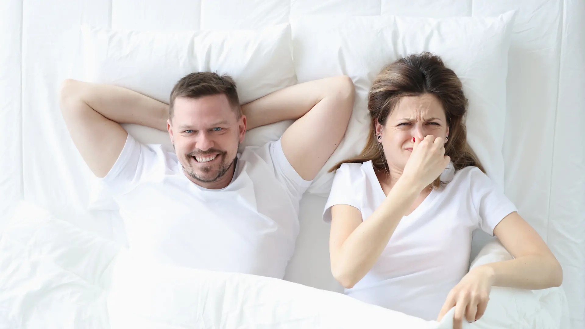 Frau liegt im Bett mit Mann und bedeckt ihre Nase mit der Hand
