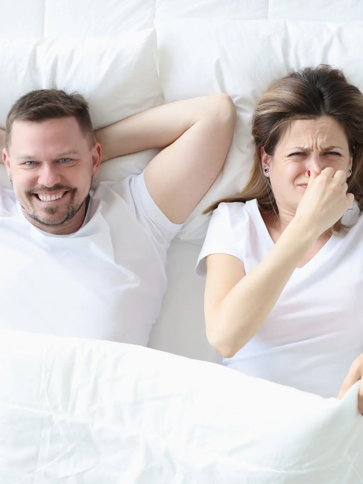 Frau liegt im Bett mit Mann und bedeckt ihre Nase mit der Hand 