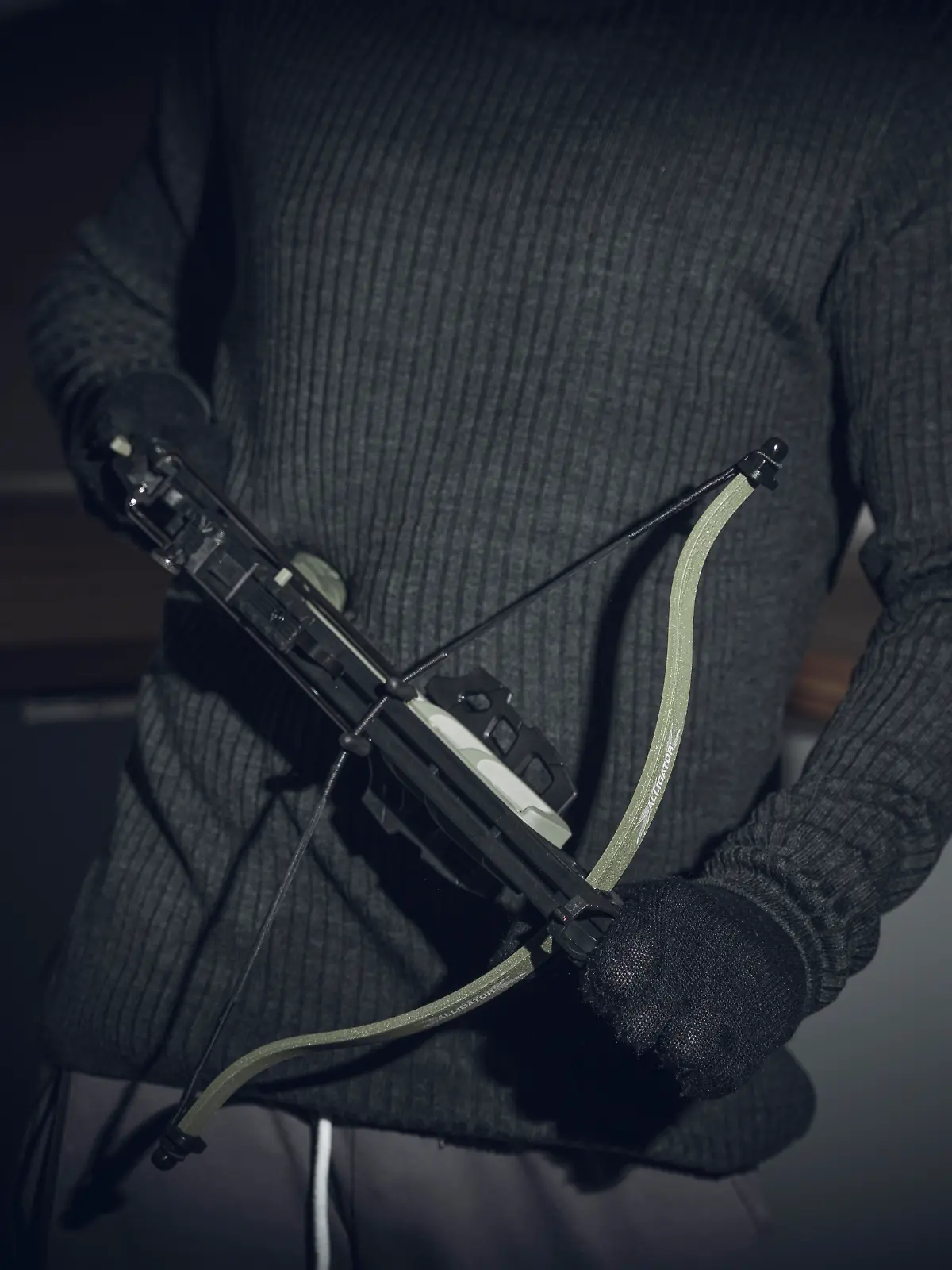 Maskierter Einbrecher in einer dunklen Wohnung mit einer Armbrust bewaffnet