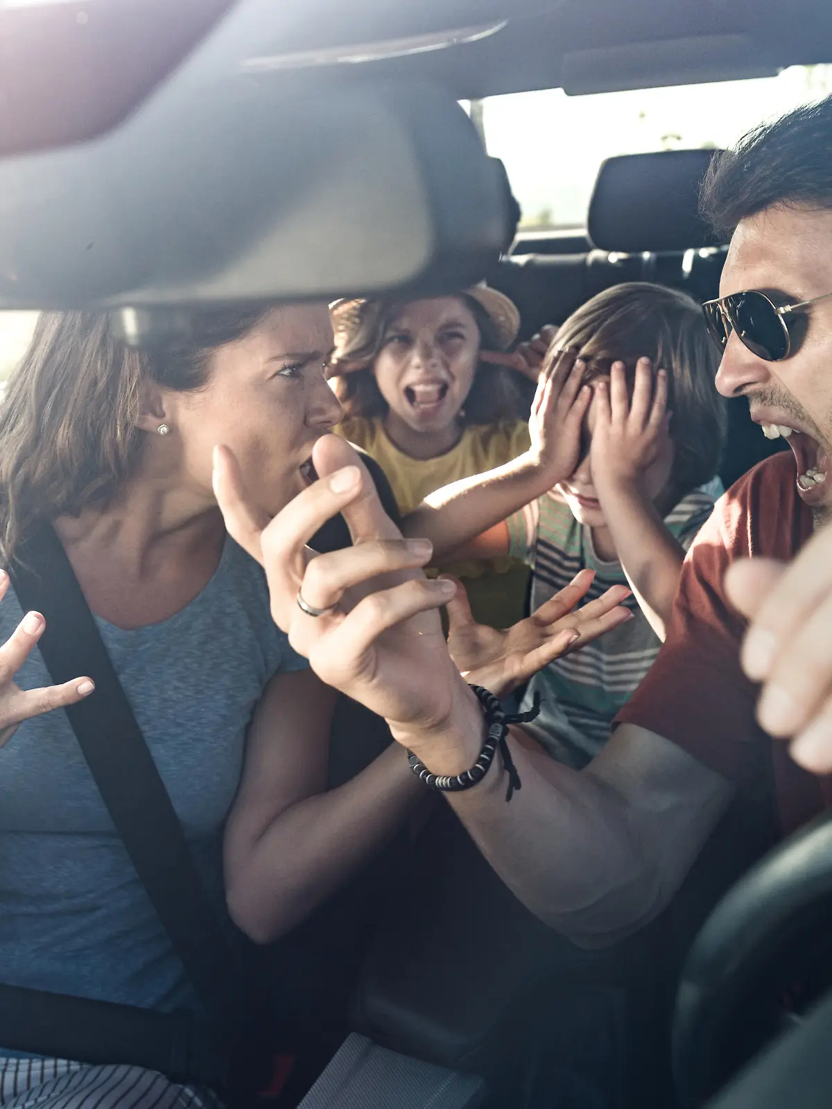 Angry parents arguing while traveling with their displeased kids in car. The view is through windshield.