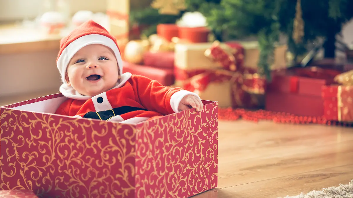 Ein Baby sitzt zu Weihnachten in einer Geschenkebox. Es trägt eine Weihnachtsmütze.