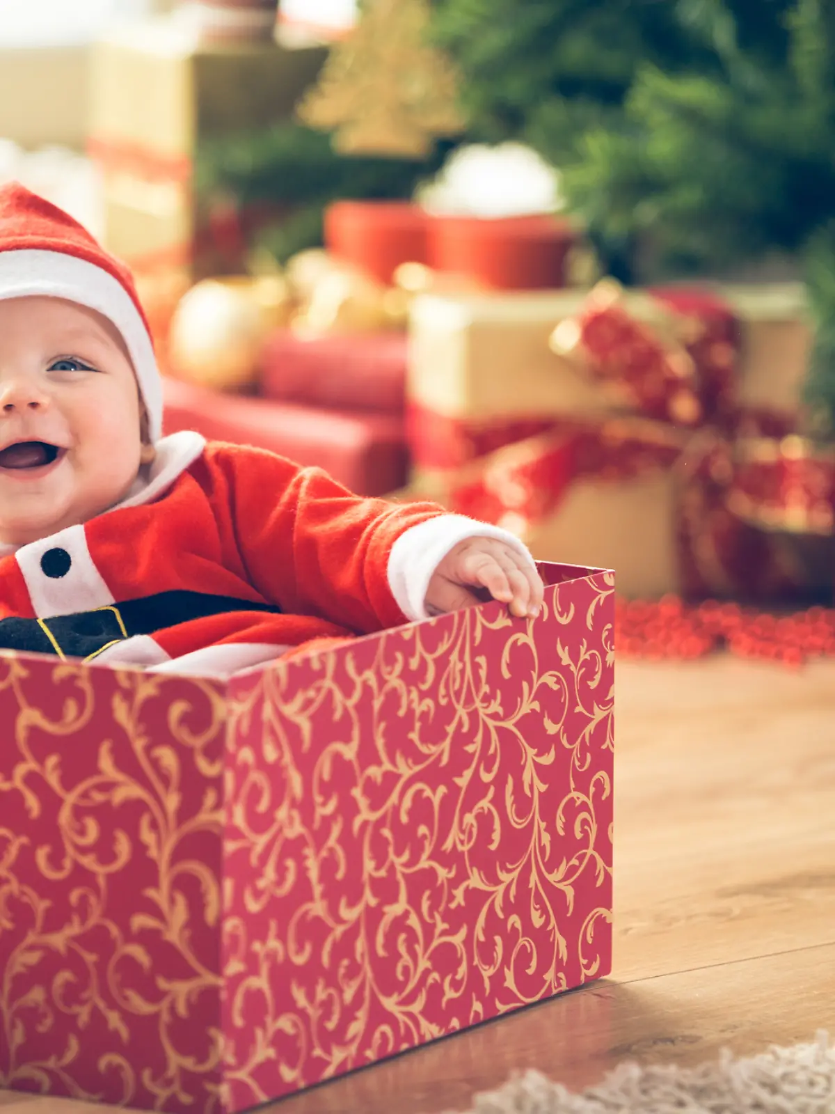 Ein Baby sitzt zu Weihnachten in einer Geschenkebox. Es trägt eine Weihnachtsmütze.