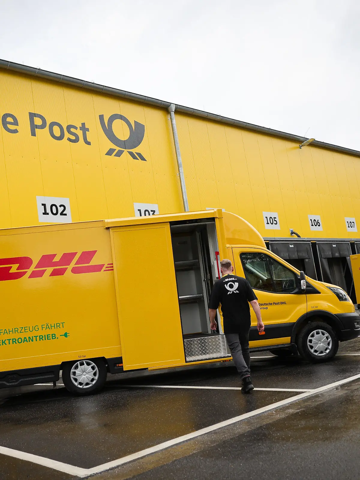 26.06.2023, Hamburg: Ein Mitarbeiter geht bei einem Fototermin zu einem elektrischen Zustellfahrzeug auf der neuen DHL-Zustellbasis. Die Deutsche Post DHL hat in Hamburg ihre bundesweit erste klimaneutrale Paket-Zustellbasis in Betrieb genommen. Die Basis im Stadtteil Schnelsen ist unter anderem mit einer Photovoltaik-Anlage, sechs Wärmepumpen für die Fußbodenheizung und 90 Ladepunkten für Elektro-Fahrzeuge ausgestattet. Foto: Christian Charisius/dpa +++ dpa-Bildfunk +++