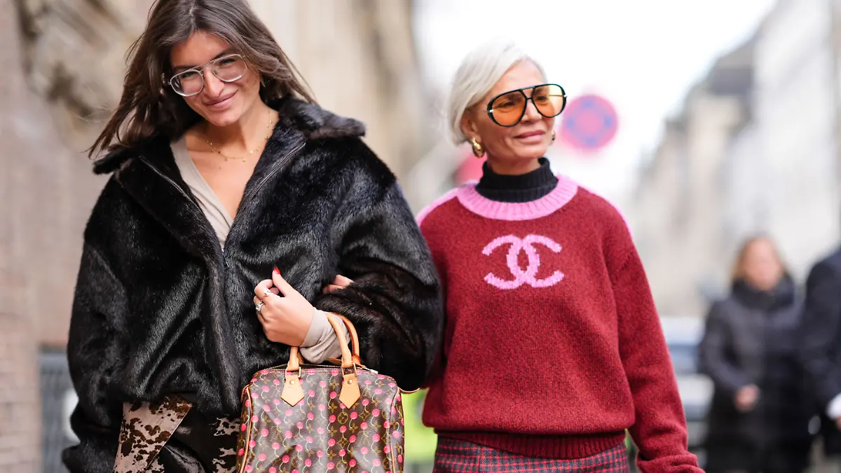 Eine braune Vuitton-Ledertasche mit Monogramm-Logo und aufgedruckten Kirschen, einen Minirock, schwarze Strumpfhosen und schwarze spitze Schuhe; Grece Ghanem (R) trägt eine Sonnenbrille, goldene Ohrringe, einen schwarzen Rollkragenpullover und ein rosa-roter Wollstrickpullover mit Chanel-Logo.