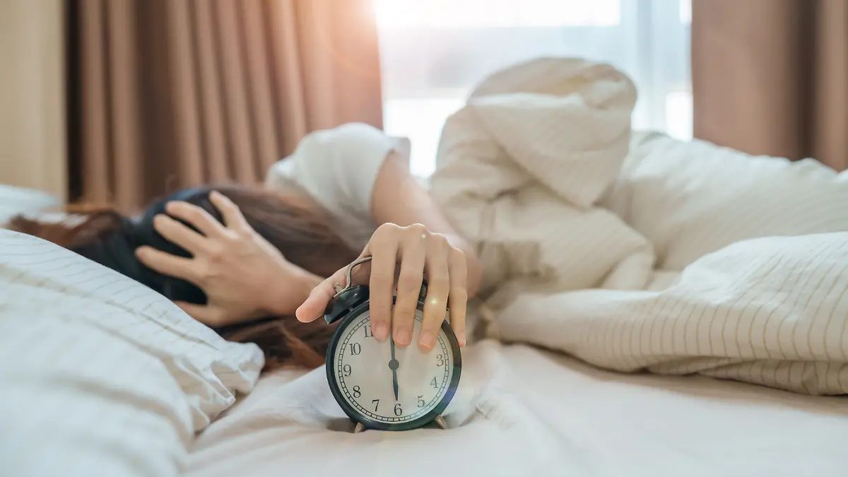 Frau liegt müde im Bett, vor ihr ein Wecker