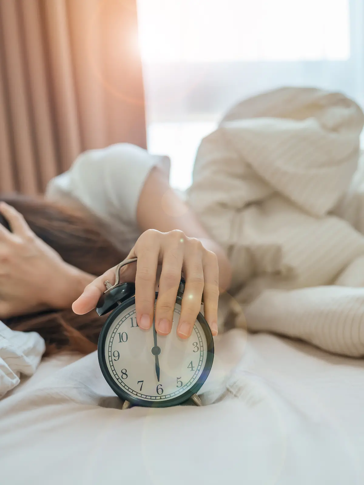 Frau liegt müde im Bett, vor ihr ein Wecker