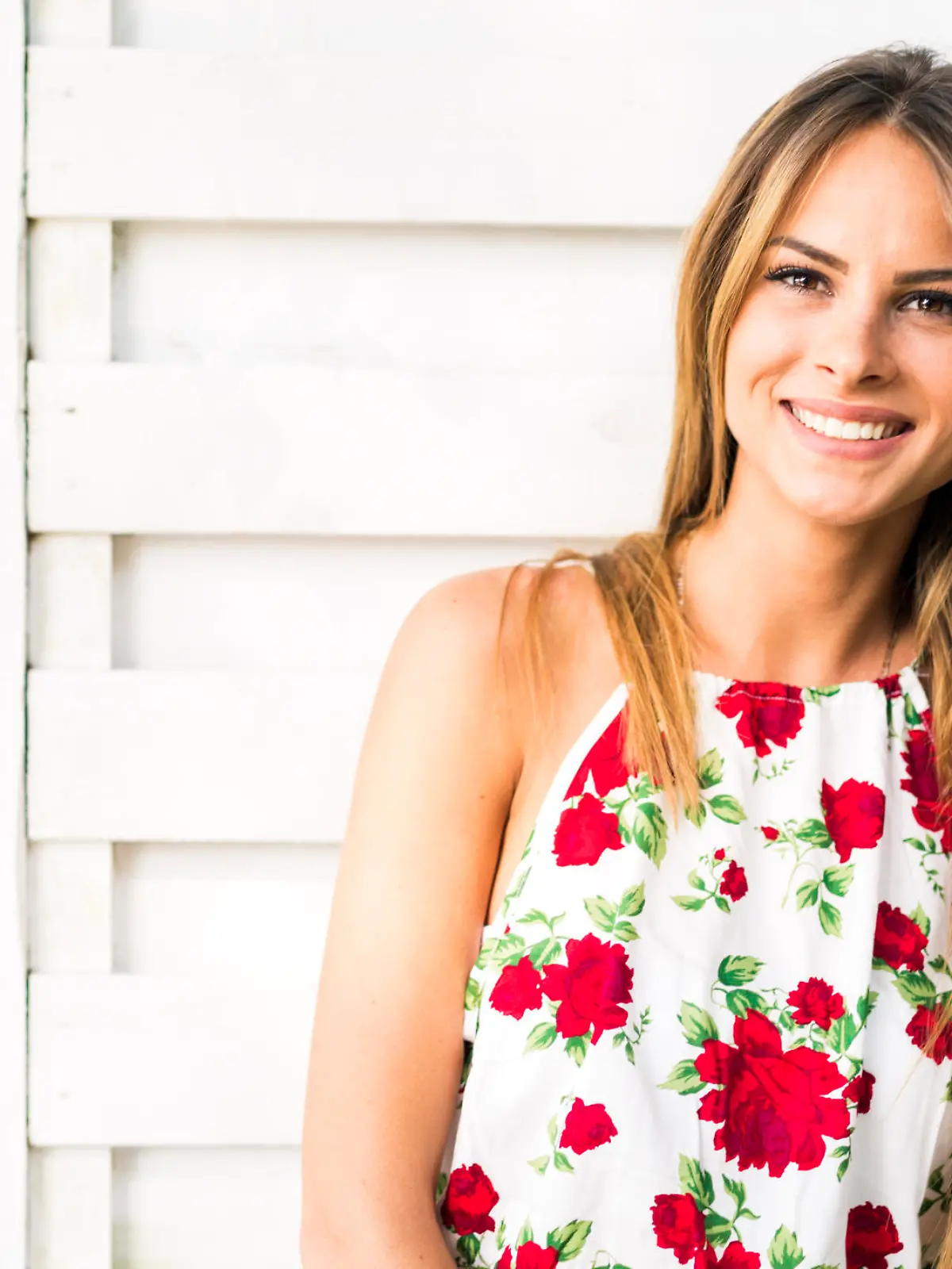 Beautiful young woman smiling outdoors with a white wooden wall in the background