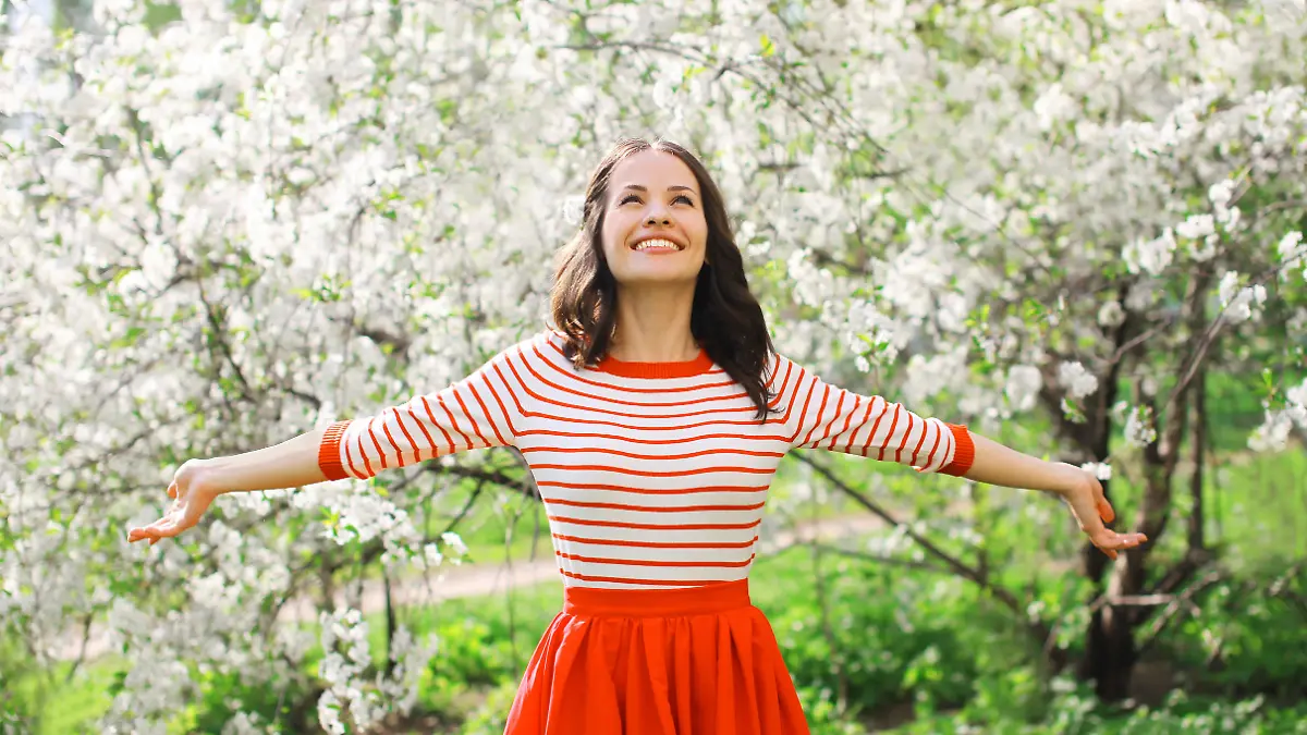 Beautiful happy young woman enjoying smell in a flowering spring garden