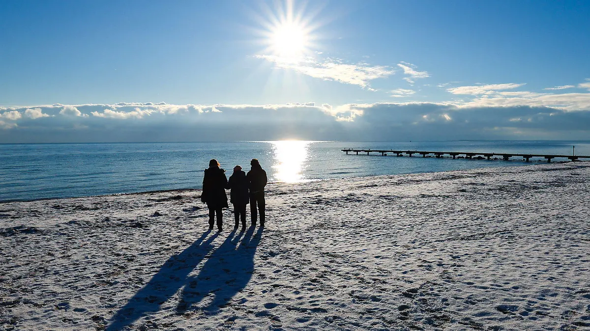 ARCHIV - 16.12.2022, Schleswig-Holstein, Burg: Drei Menschen gehen am Südstrand bei Burg auf Fehmarn im strahlenden Sonnenschein spazieren. Der Sandstrand ist mit einer dünnen Schneedecke bedeckt. Die Ferienorte Schleswig-Holsteins sind über die Feiertage und den Jahreswechsel wieder gut gebucht. (zu dpa: «Schleswig-Holstein zu Weihnachten und Silvester sehr nachgefragt») Foto: Christian Charisius/dpa +++ dpa-Bildfunk +++