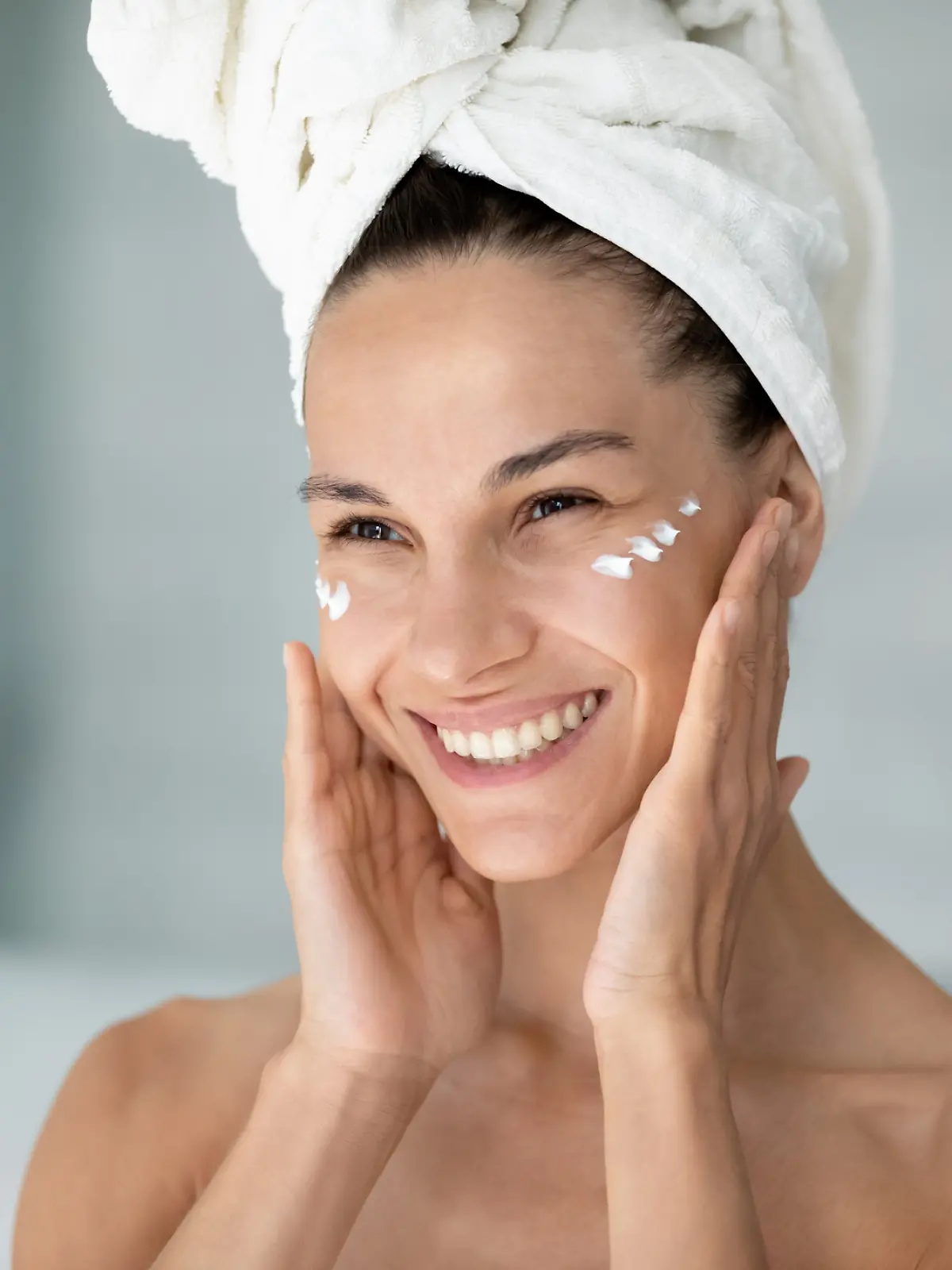 Eine Frau cremt sich nach dem Duschen das Gesicht ein. Sie nutzt eine Anti-Aging-Pflege.