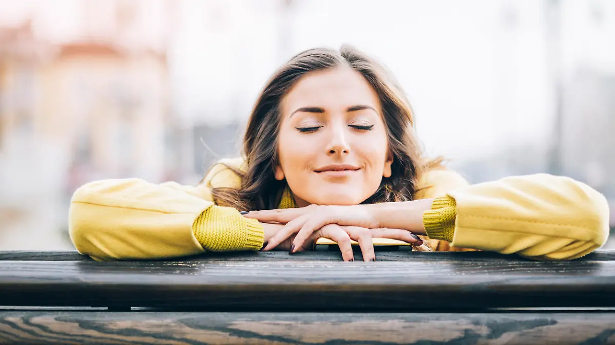 Beautiful young woman sitting on a bench enjoying the sunlight outdoors in the city, with copy space