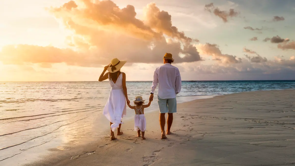 A elegant family in white summer clothing walks hand in hand down a tropical paradise beach during sunset tme and enjoys their vacation time