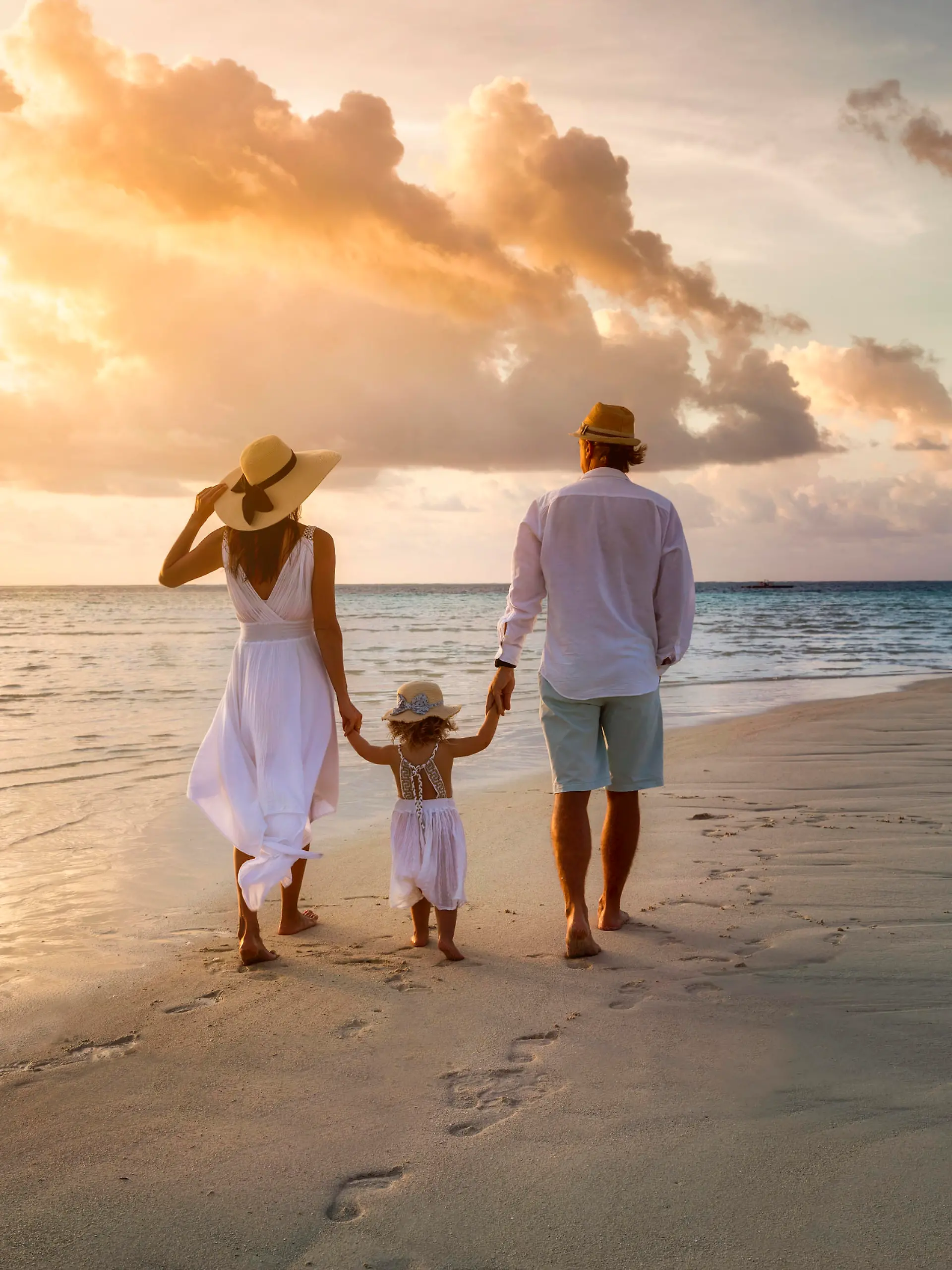 A elegant family in white summer clothing walks hand in hand down a tropical paradise beach during sunset tme and enjoys their vacation time