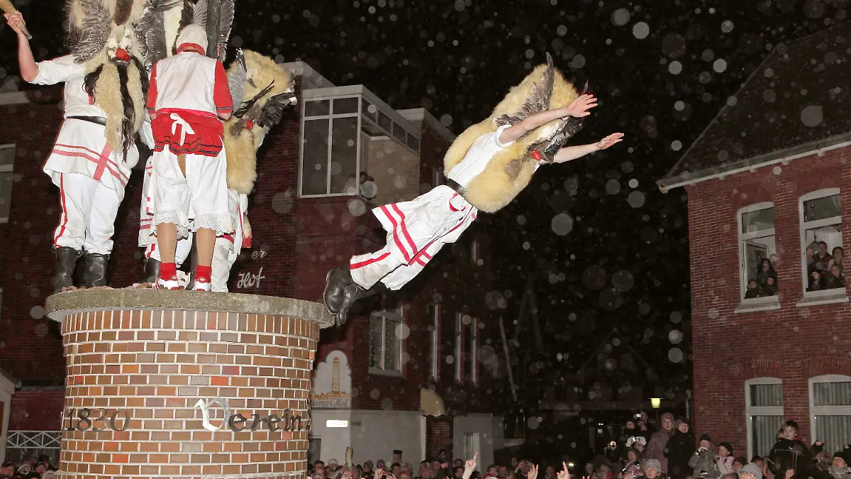 Mit Masken verkleidete Männer des Vereins Borkumer Jungens stürzen sich am Abend (Aufnahme vom 05.12.2011) in der Innenstadt der Nordseeinsel von einer Litfaßsäule in die Arme der Schaulustigen.