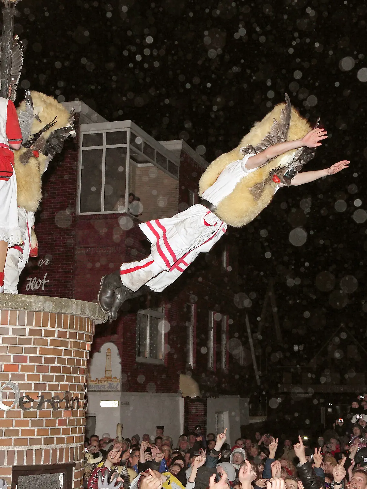 Mit Masken verkleidete Männer des Vereins Borkumer Jungens stürzen sich am Abend (Aufnahme vom 05.12.2011) in der Innenstadt der Nordseeinsel von einer Litfaßsäule in die Arme der Schaulustigen.