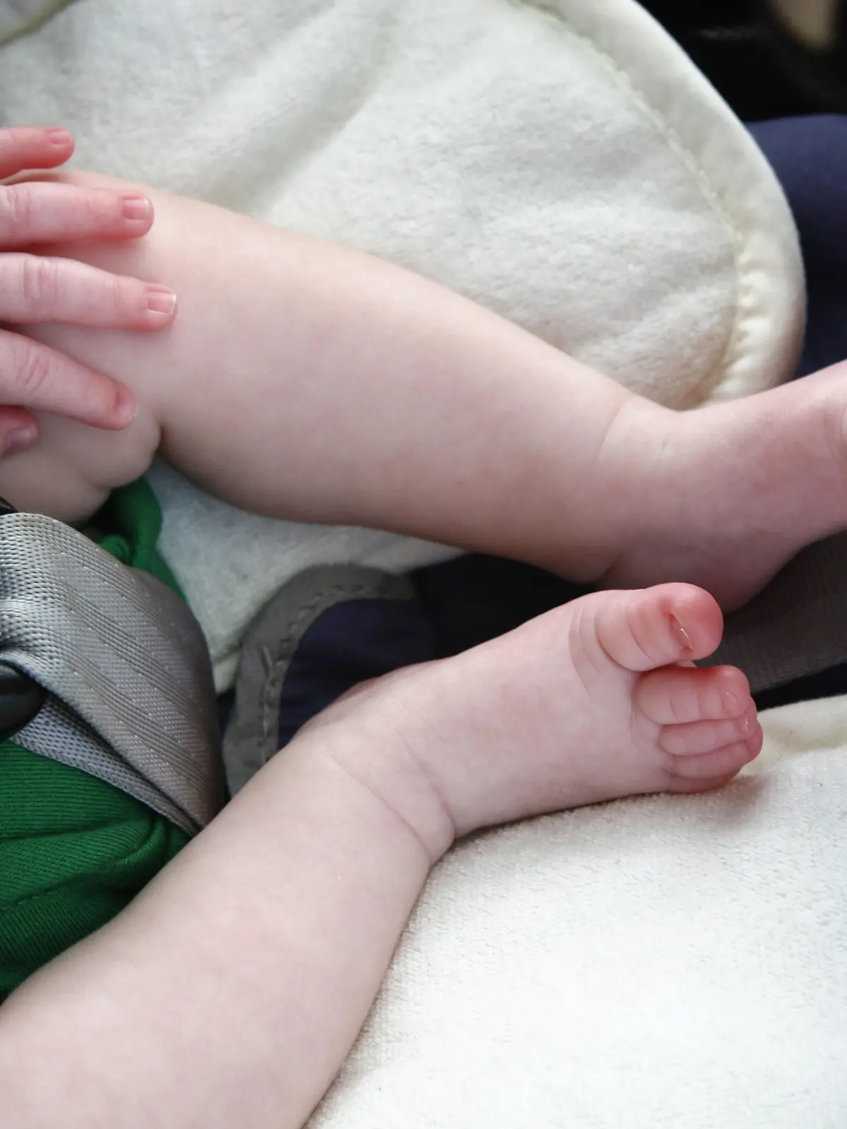 Legs and hand of little child in car seat.