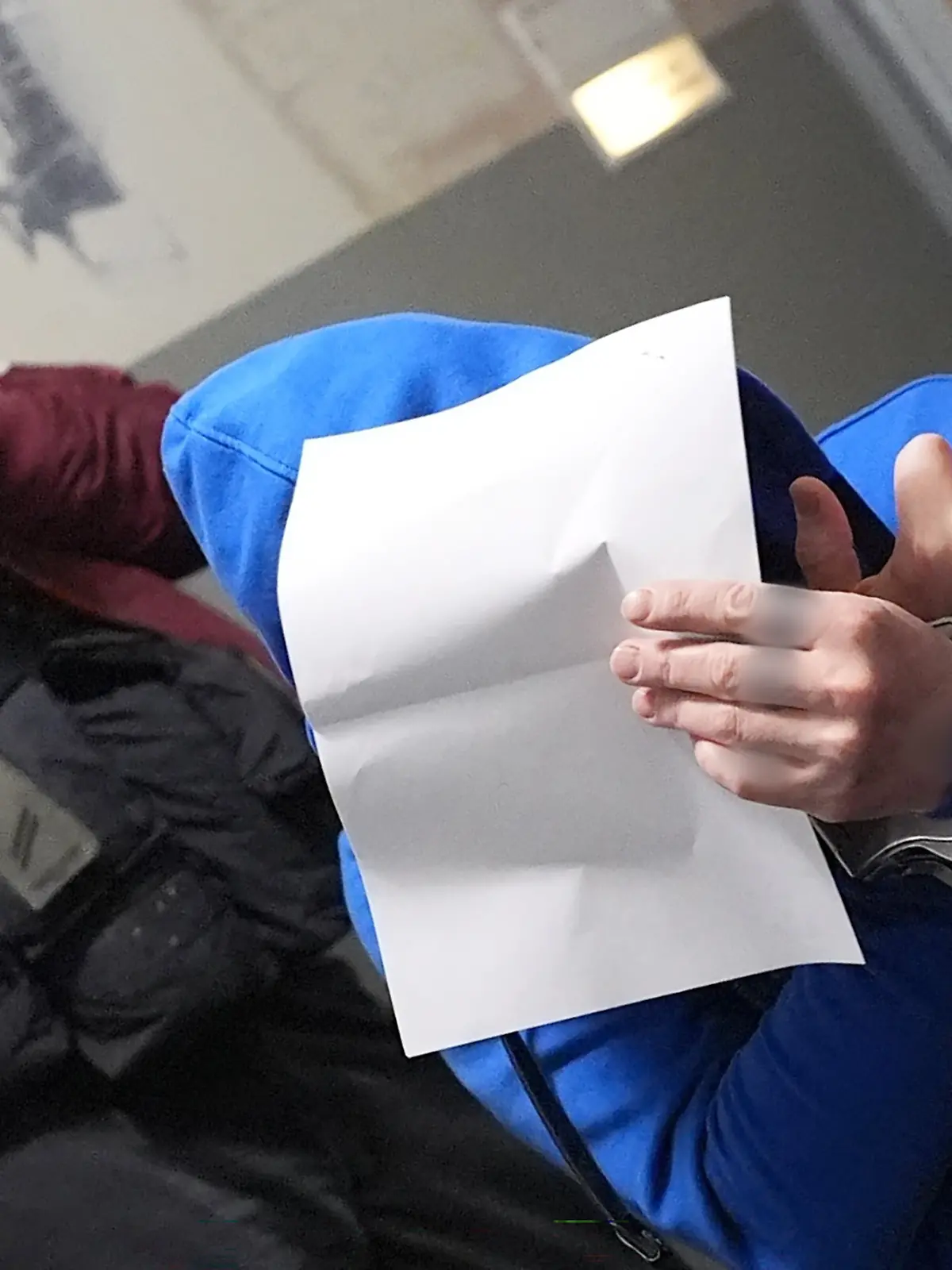 Schleswig-Holstein, Flensburg: Ein Angeklagter hält sich ein Blatt Papier vor sein Gesicht und zeigt dabei den Mittelfinger seiner rechten Hand auf dem Flur des Landgerichts, nach dem ersten Sitzungstag im Mordprozess. Vier Angeklagte sollen gemeinsam am 11. Januar 2024 ein Seniorenpaar in St. Peter-Ording brutal in dessen Haus überfallen haben.