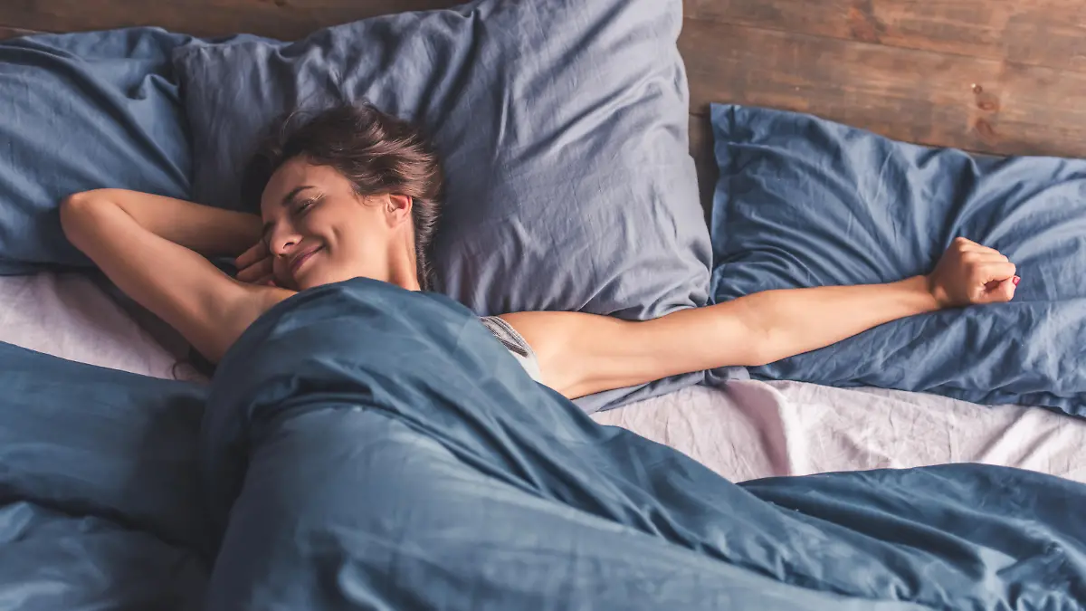Beautiful young woman is stretching and smiling while lying in bed in the morning