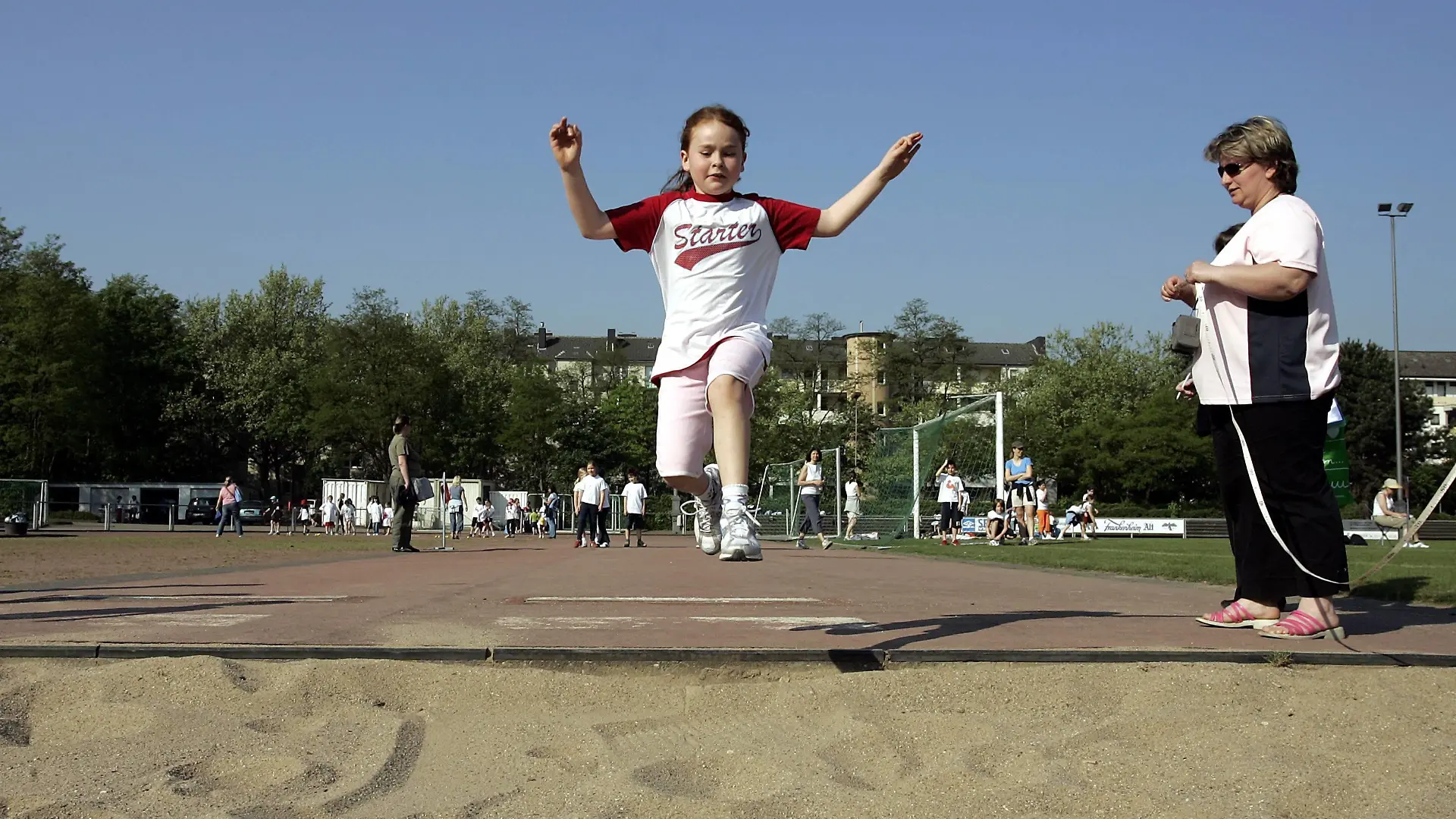 Junges Mädchen bei einem Weitsprungversuch im Rahmen der Bundesjugendspiele in der Flugphase
young Girl at a Long jump attempt in frame the Federal Youth Games in the Flight phase