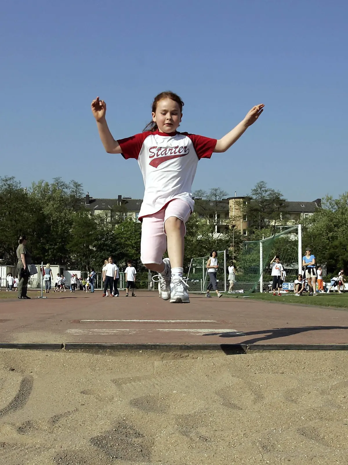 Junges Mädchen bei einem Weitsprungversuch im Rahmen der Bundesjugendspiele in der Flugphase

young Girl at a Long jump attempt in frame the Federal Youth Games in the Flight phase