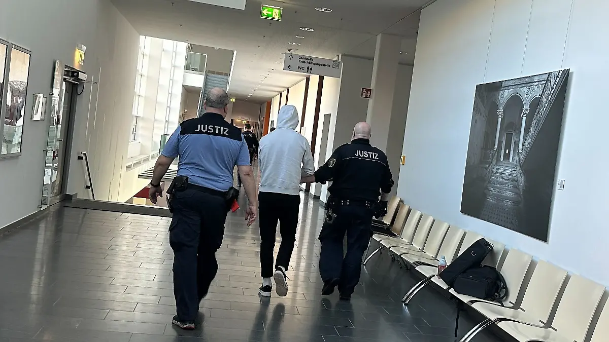 Ein Mann wird im Gericht von zwei Beamten flankiert und durch den Flur geführt. 