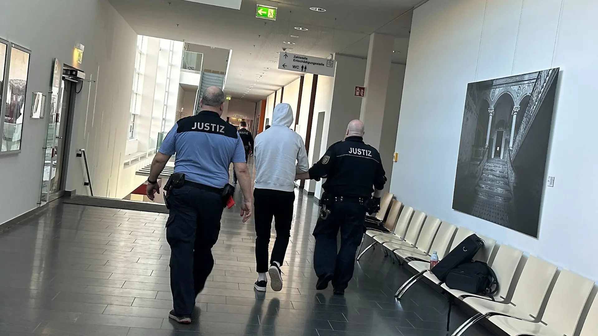 Ein Mann wird im Gericht von zwei Beamten flankiert und durch den Flur geführt.