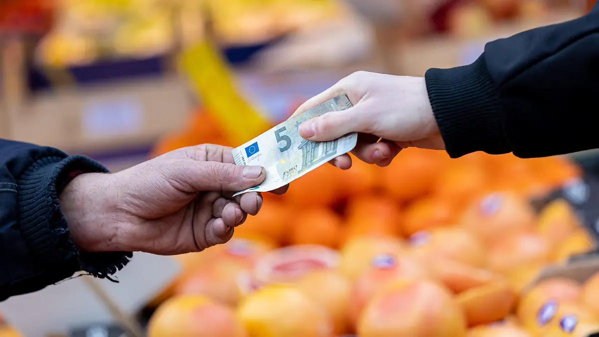 ARCHIV - 29.01.2022, Niedersachsen, Hannover: ILLUSTRATION - Ein Kunde bezahlt seinen Einkauf an einem Stand auf einem Wochenmarkt mit einem Fünf-Euro-Schein (gestellte Szene). Die Lebensmittelpreise steigen deutlich. Nun gibt es in der EU neue rechtliche Möglichkeiten zur Senkung der Mehrwertsteuer.(zu dpa: «Verbände fordern Mehrwertsteuersenkung auf Null bei Lebensmitteln») Foto: Moritz Frankenberg/dpa +++ dpa-Bildfunk +++