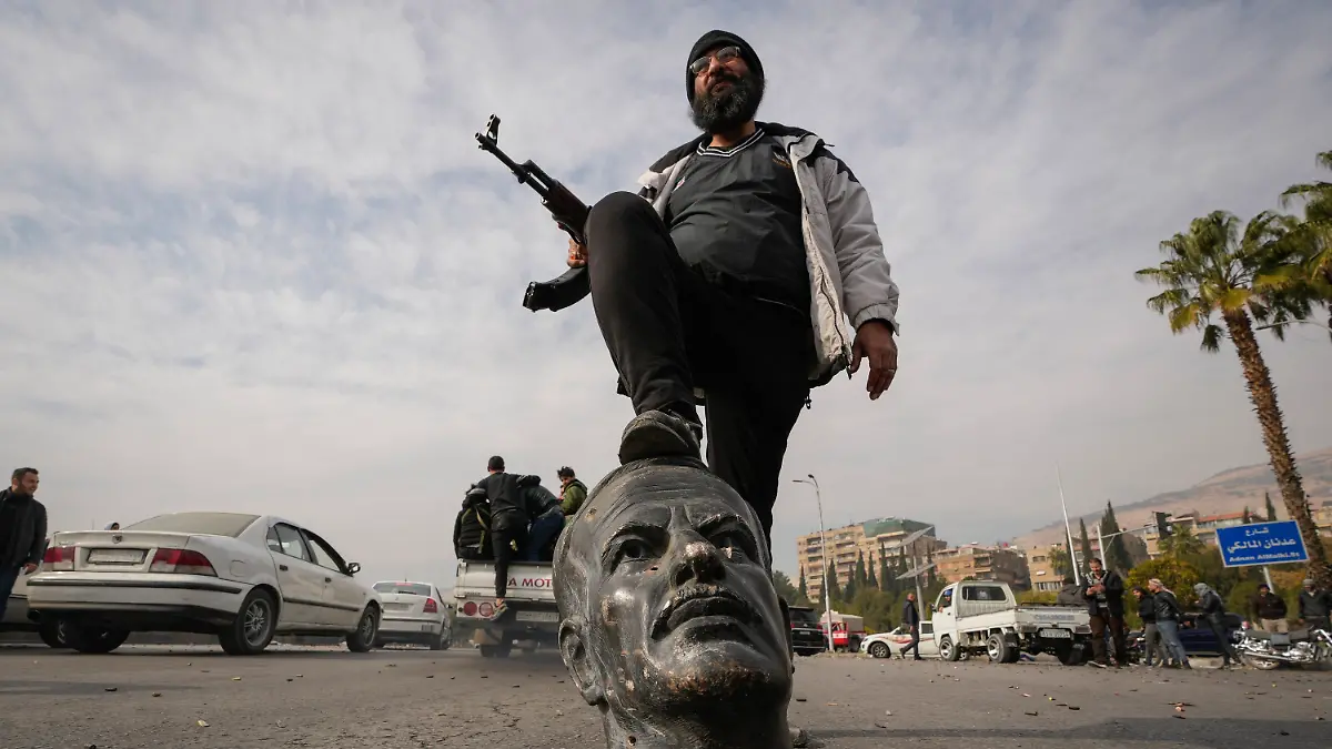 dpatopbilder - 08.12.2024, Syrien, Damaskus: Ein Oppositionskämpfer tritt auf den abgetrennten Kopf einer Statue des gestorbenen syrischen Präsidenten Hafis al-Assad. Foto: Hussein Malla/AP/dpa +++ dpa-Bildfunk +++
