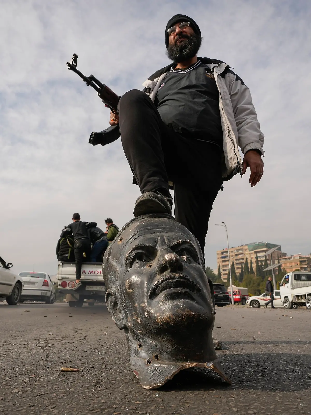 dpatopbilder - 08.12.2024, Syrien, Damaskus: Ein Oppositionskämpfer tritt auf den abgetrennten Kopf einer Statue des gestorbenen syrischen Präsidenten Hafis al-Assad. Foto: Hussein Malla/AP/dpa +++ dpa-Bildfunk +++