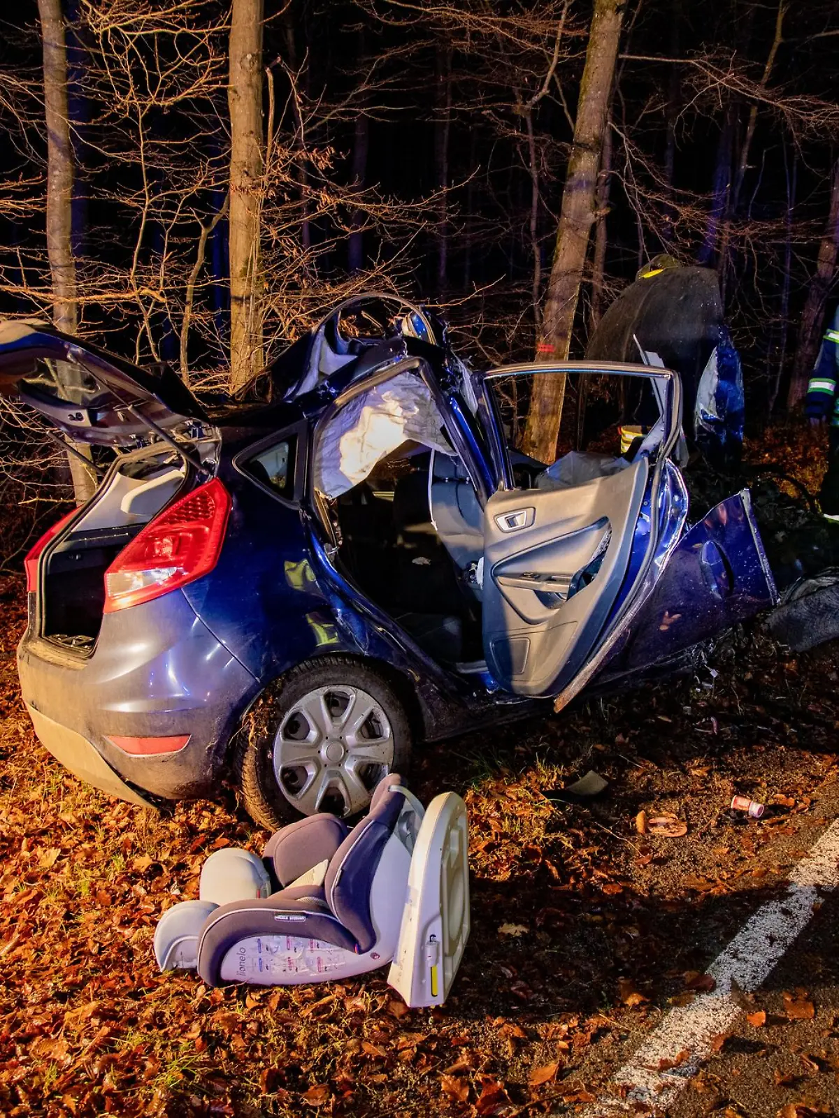 Feuerwehrmänner stehen neben einem verunglückten Auto. Ein mit vier jungen Menschen besetztes Auto ist im Vogelsbergkreis mit einem Baum zusammengestoßen und ein 17-jähriger Beifahrer gestorben.