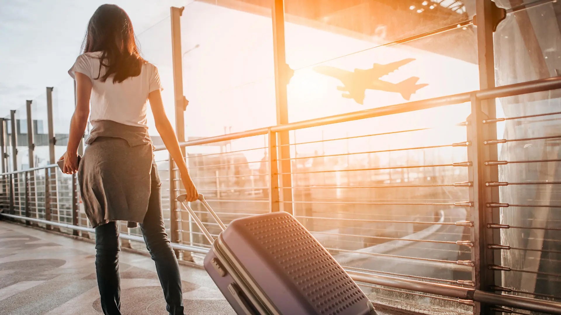 Young woman pulling suitcase in airport terminal. Copy space