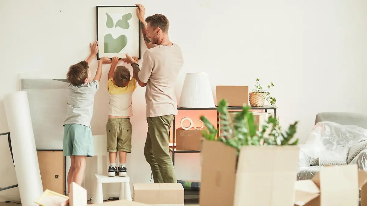 Full length portrait of happy father with two sons hanging pictures on wall while moving in to new home, copy space