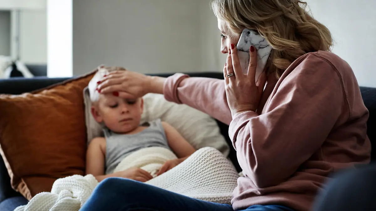 Shot of a mother wearing a surgical mask making a phone call while aiding to her sick young son at home