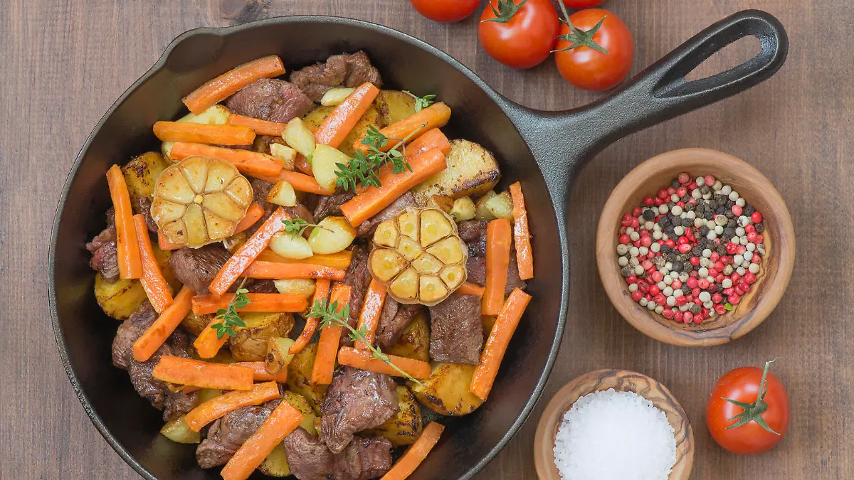 Roasted meat with vegetables in a cast iron skillet on a wooden table