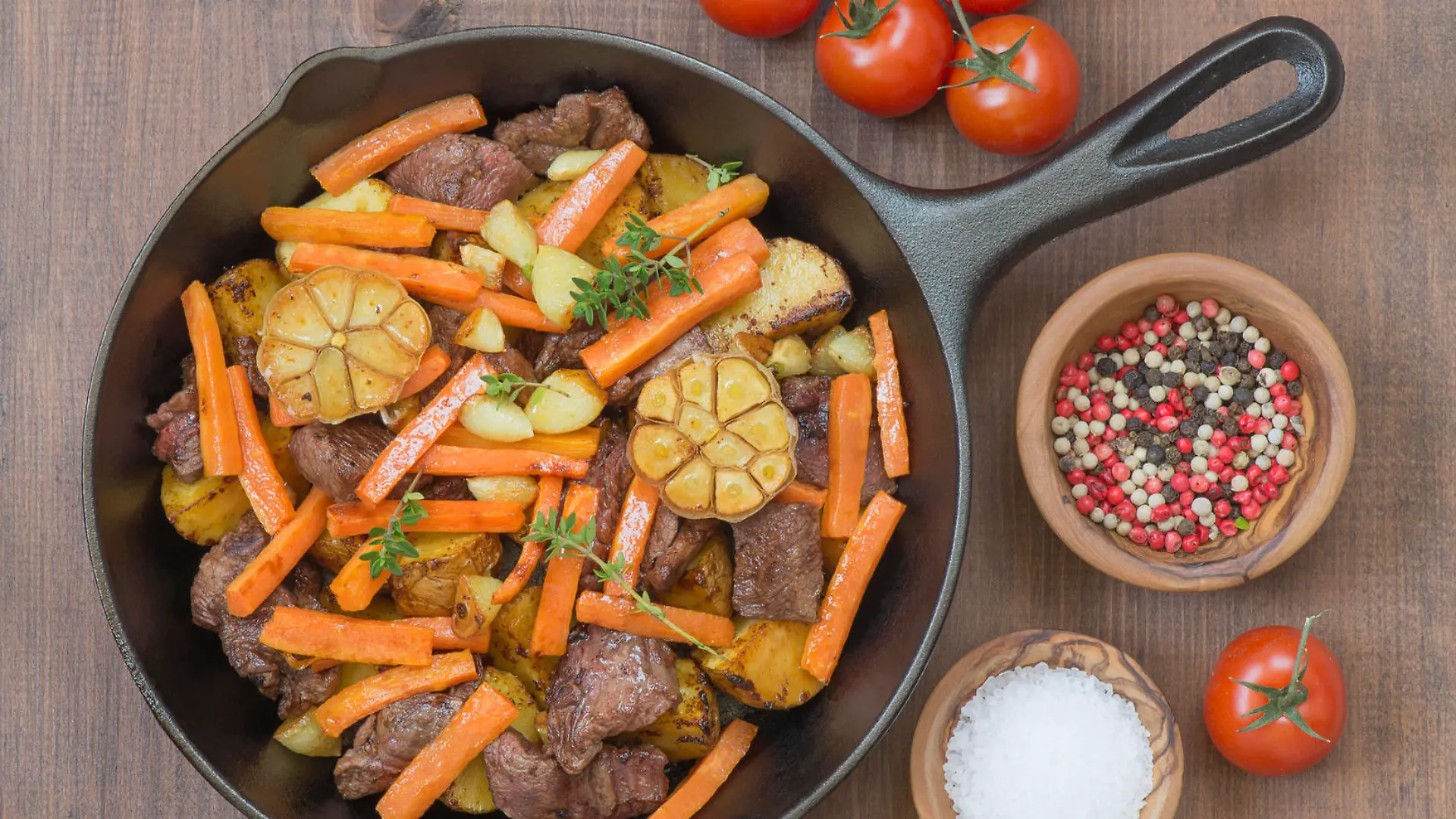 Roasted meat with vegetables in a cast iron skillet on a wooden table