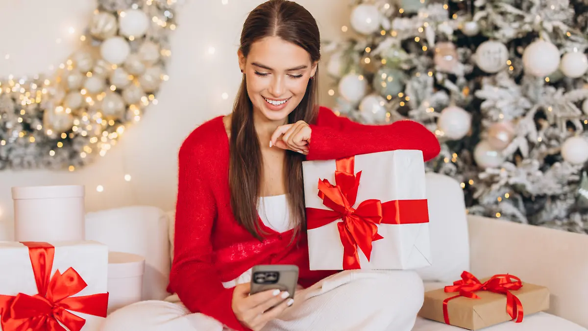 Eine Frau sitzt in weihnachtlicher Kulisse auf dem Boden und schaut auf ihr Smartphone.