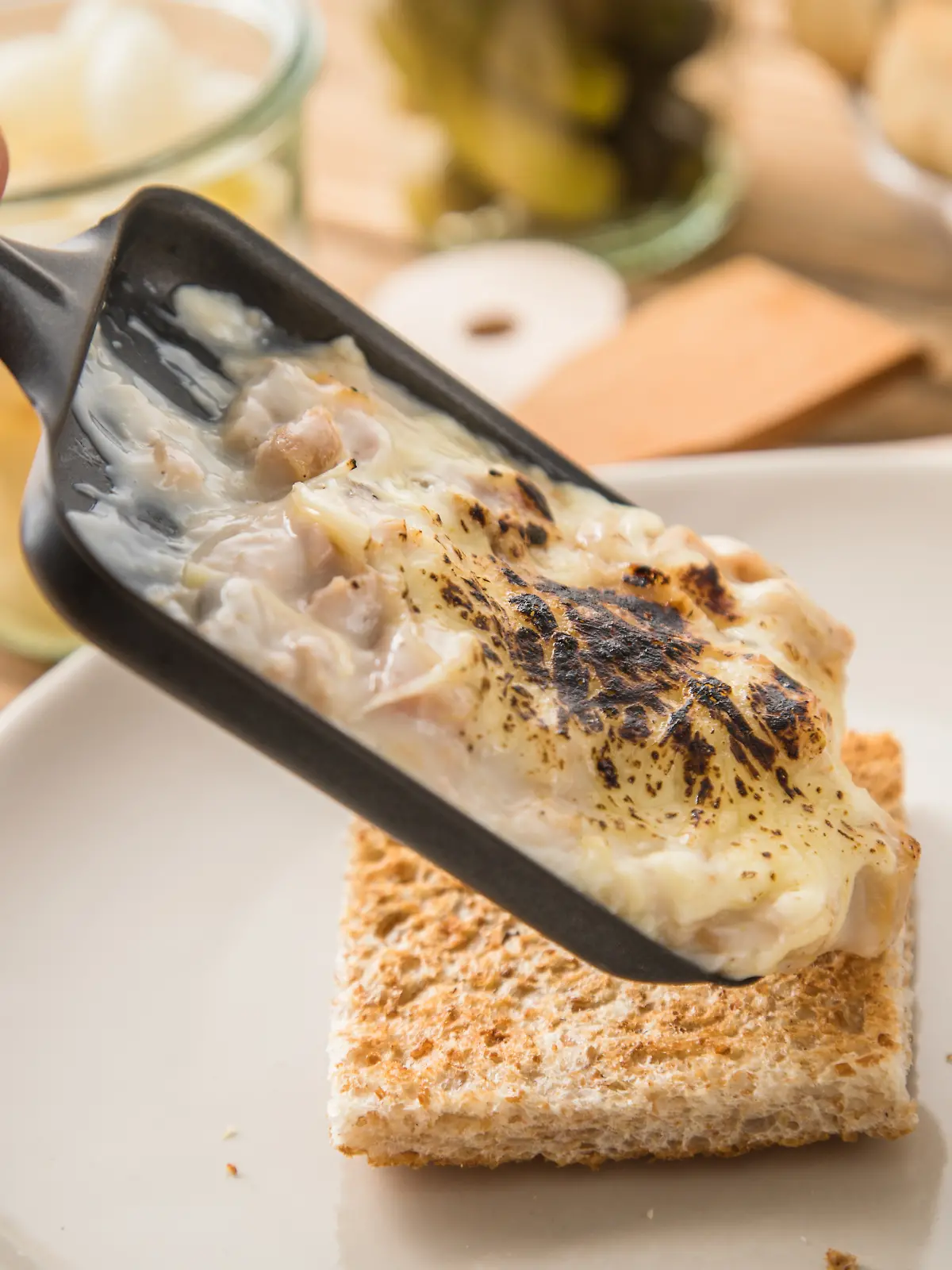 Von einem Raclette-Pfännchen läuft zerschmolzener Käse auf Brot.