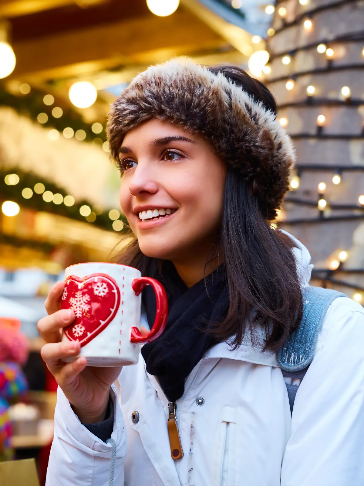 Frau steht mit Glühweintasse in der Hand auf einem Weihnachtsmarkt