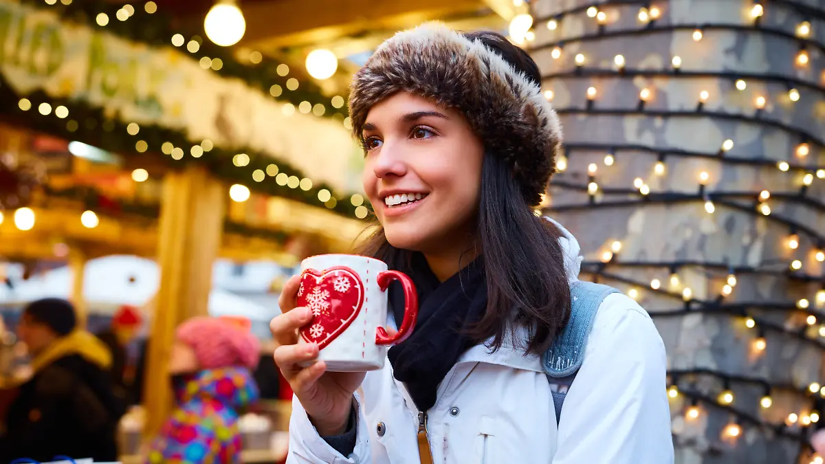 Frau steht mit Glühweintasse in der Hand auf einem Weihnachtsmarkt.