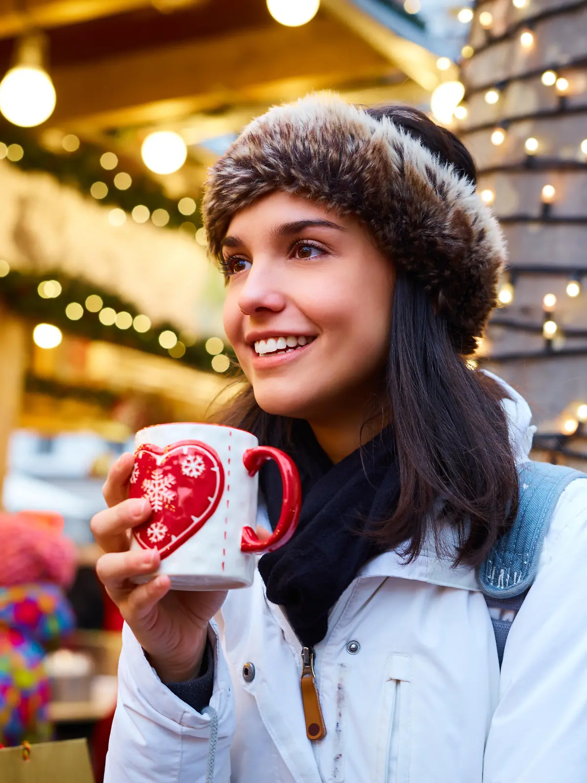 Frau steht mit Glühweintasse in der Hand auf einem Weihnachtsmarkt.