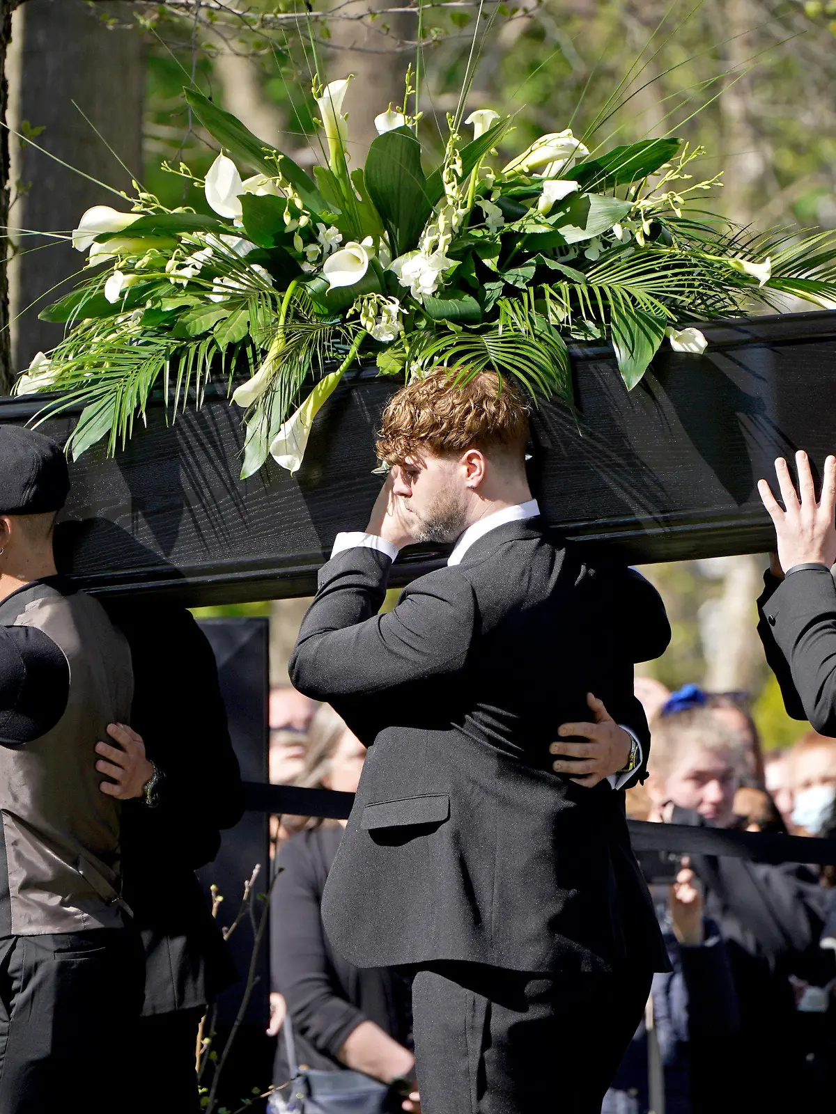 20.04.2022, Großbritannien, London: Max George (l) und Jay McGuiness (M), Mitglieder der Band «The Wanted», tragen den Sarg von Parker in die Kirche. Der britische Sänger Tom Parker von der Boygroup «The Wanted» war 17 Monate nach einer Diagnose eines inoperablen Hirntumors im Alter von 33 Jahren gestorben. Foto: Kirsty O'connor/PA Wire/dpa +++ dpa-Bildfunk +++