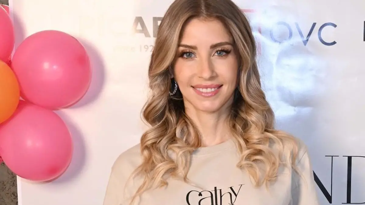17.06.2023, Bayern, München: Moderatorin Cathy Hummels steht lächelnd in ihrer alten Wohnung in München-Bogenhausen vor einer Plakatwand mit der Aufschrift Secondhand Summer Bazaar by Cathy Hummels", während sie im Rahmen eines privaten Flohmarkts Möbel und Kleidungsstücke verkauft, die sie bei ihrem Umzug aussortiert hat. Der Erlös soll anteilig an eine Hilfsorganisation für Kinder gespendet werden. Foto: Felix Hörhager/dpa +++ dpa-Bildfunk +++