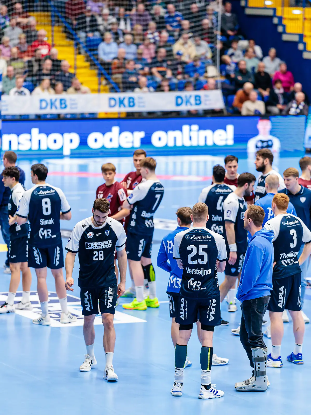 Die Spieler des TBV Lemgo und VfL Potsdam stehen auf dem Platz und warten auf Informationen.