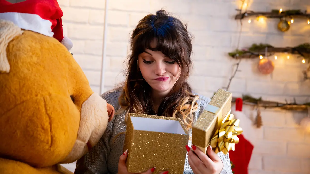 Geschenke-Fehler: Junge Frau öffnet ein Geschenk und guckt enttäuscht.